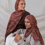 Two women wearing red clay ripple printed hijabs sitting against a plain background