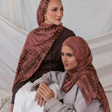Two women wearing red clay ripple printed hijabs sitting against a plain background