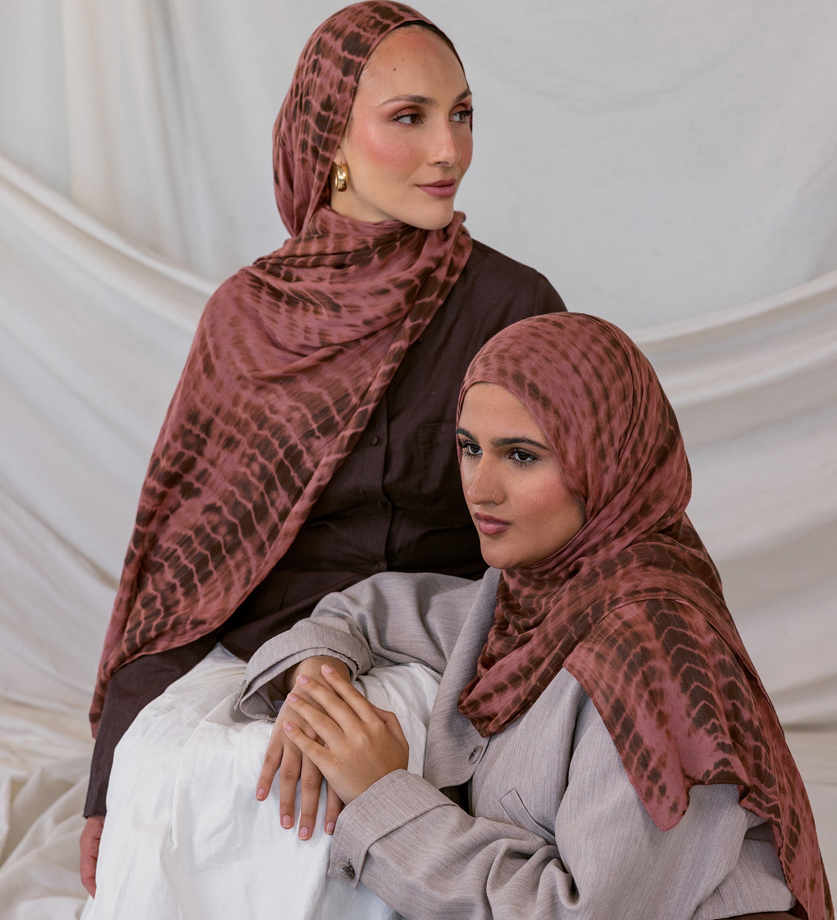 Two women wearing red clay ripple printed hijabs sitting against a plain background