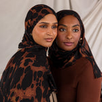 Two women styled in tortoiseshell patterned hijabs against a plain background