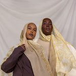 Two women wearing yellow and tan printed headscarves against a plain background