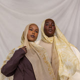 Two women wearing yellow and tan printed headscarves against a plain background