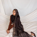 Woman laying the Chocolate Paisley hijab on her side to reach the ground in studio lighting.