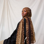 Fawn print depicted styled on model, this scarf features warm brown tones with white spots that resemble a fawn print. 
