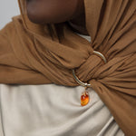 Close-up of a person wearing a brown hijab with a gold ring and mango shaped gemstone pendant.