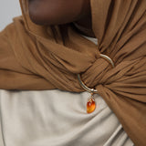 Close-up of a person wearing a brown hijab with a gold ring and mango shaped gemstone pendant.