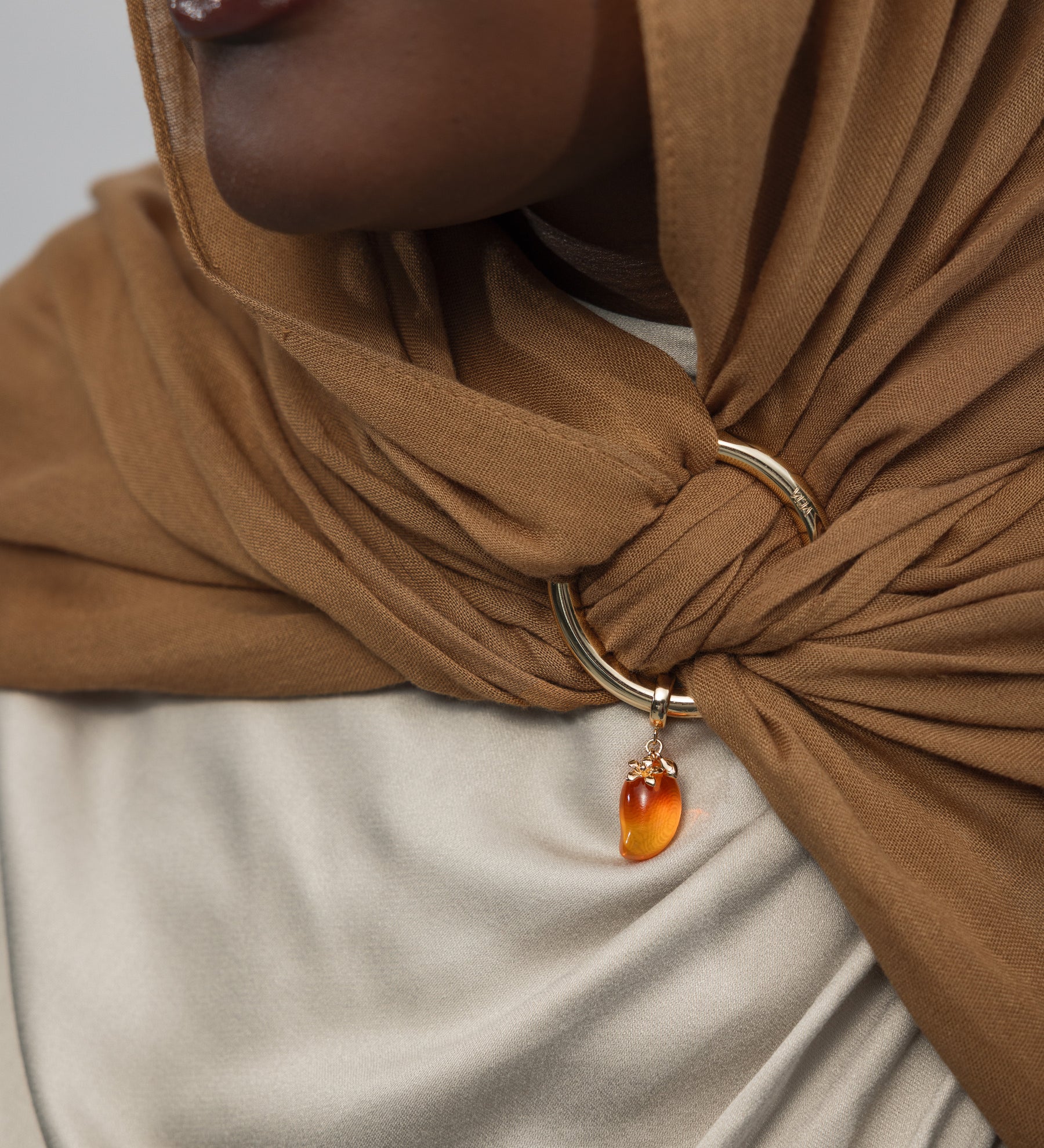 Close-up of a person wearing a brown hijab with a gold ring and mango shaped gemstone pendant.