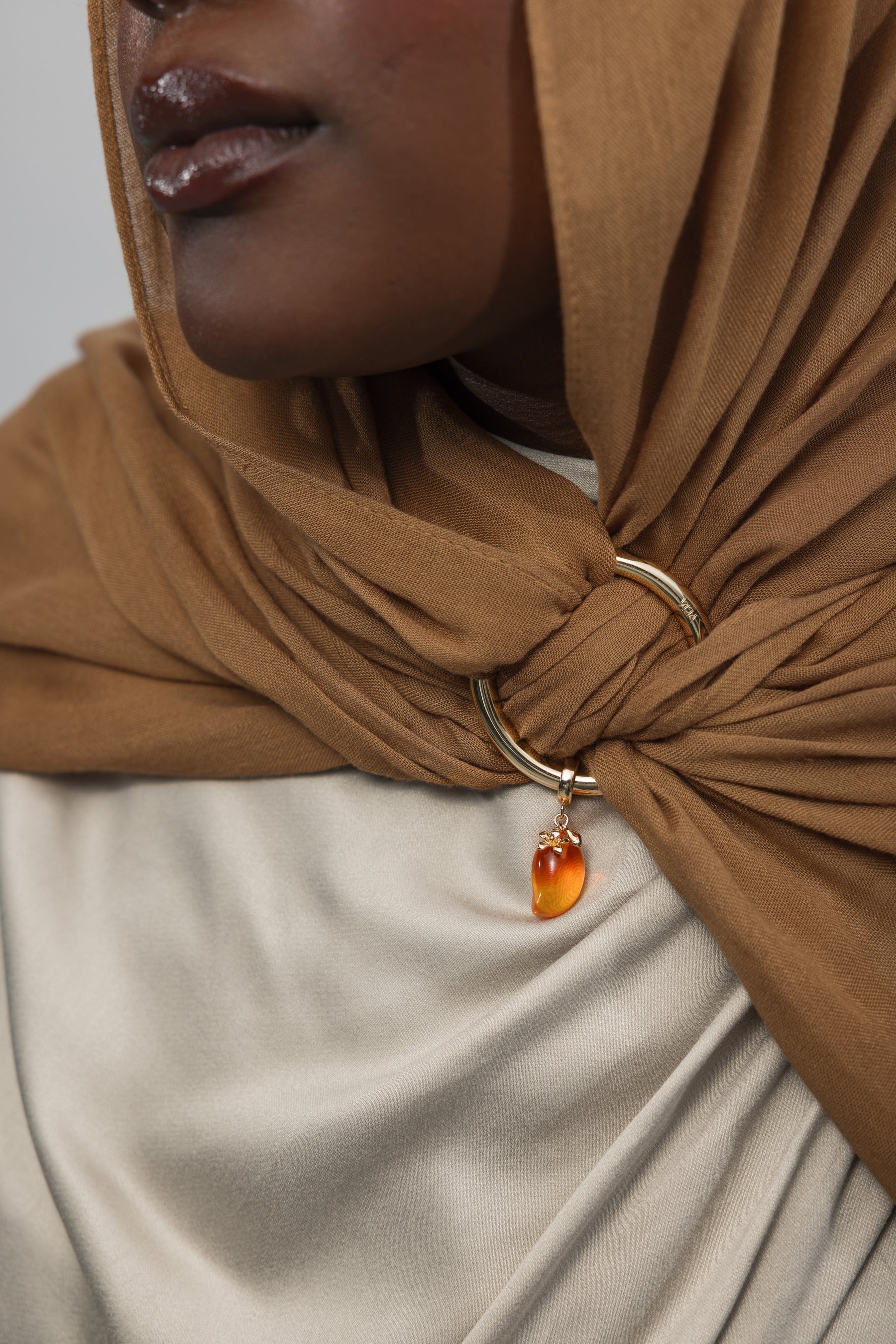 Close-up of a person wearing a brown hijab with a gold ring and mango shaped gemstone pendant.