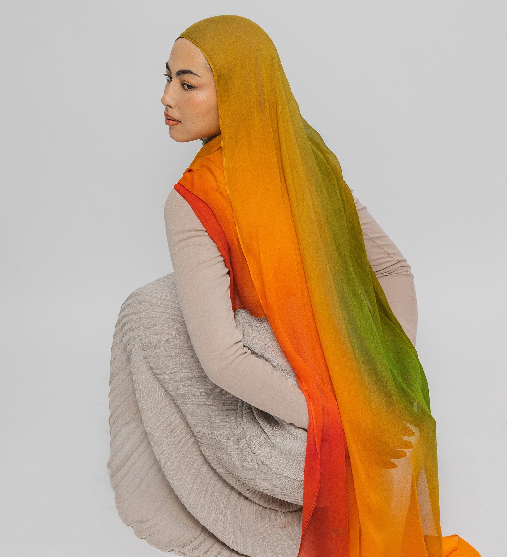 Person wearing a mango hijab with an ombre effect on a plain background