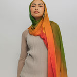 Woman wearing a ombre hijab with a gradient of green, orange, and red on a plain background