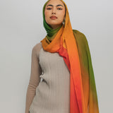 Woman wearing a ombre hijab with a gradient of green, orange, and red on a plain background