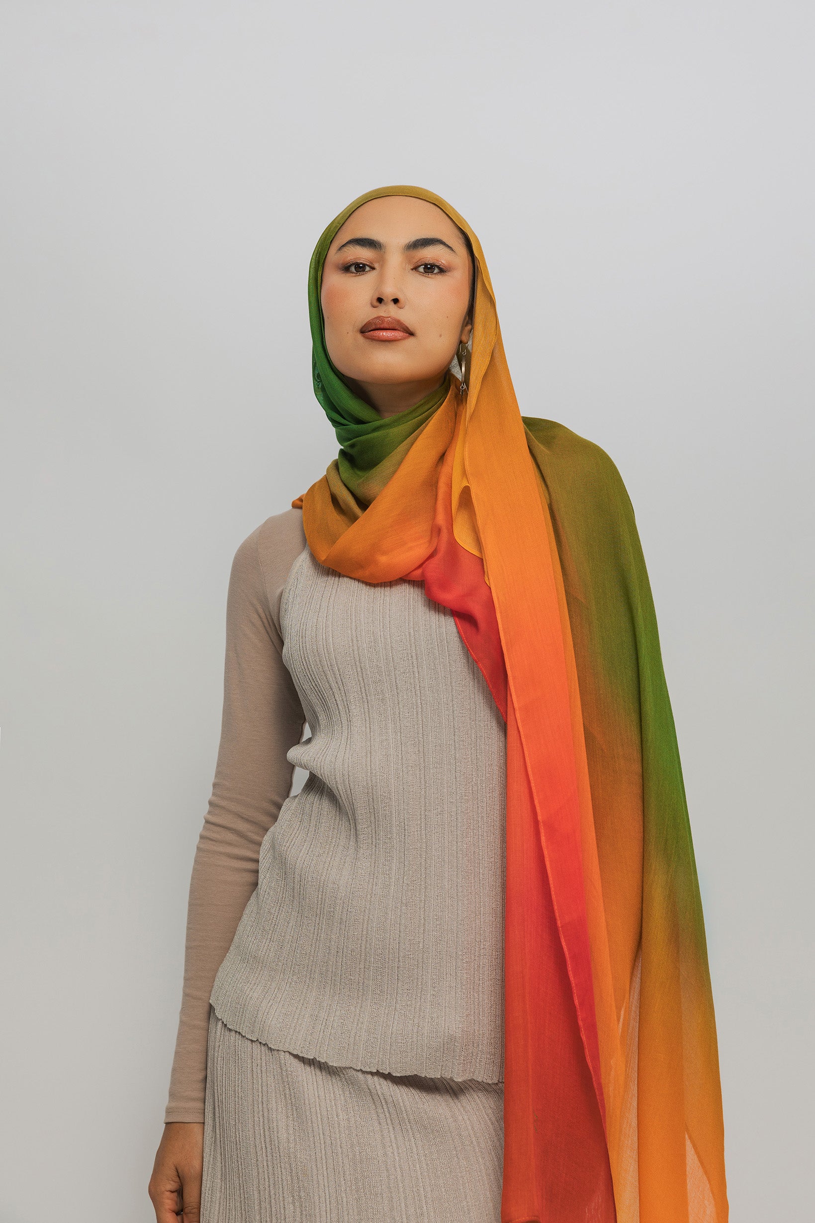 Woman wearing a ombre hijab with a gradient of green, orange, and red on a plain background