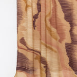 A close-up of a draped fabric with an abstract, textured pattern in shades of beige, brown, and muted pink on a plain white background.