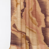 A close-up of a draped fabric with an abstract, textured pattern in shades of beige, brown, and muted pink on a plain white background.