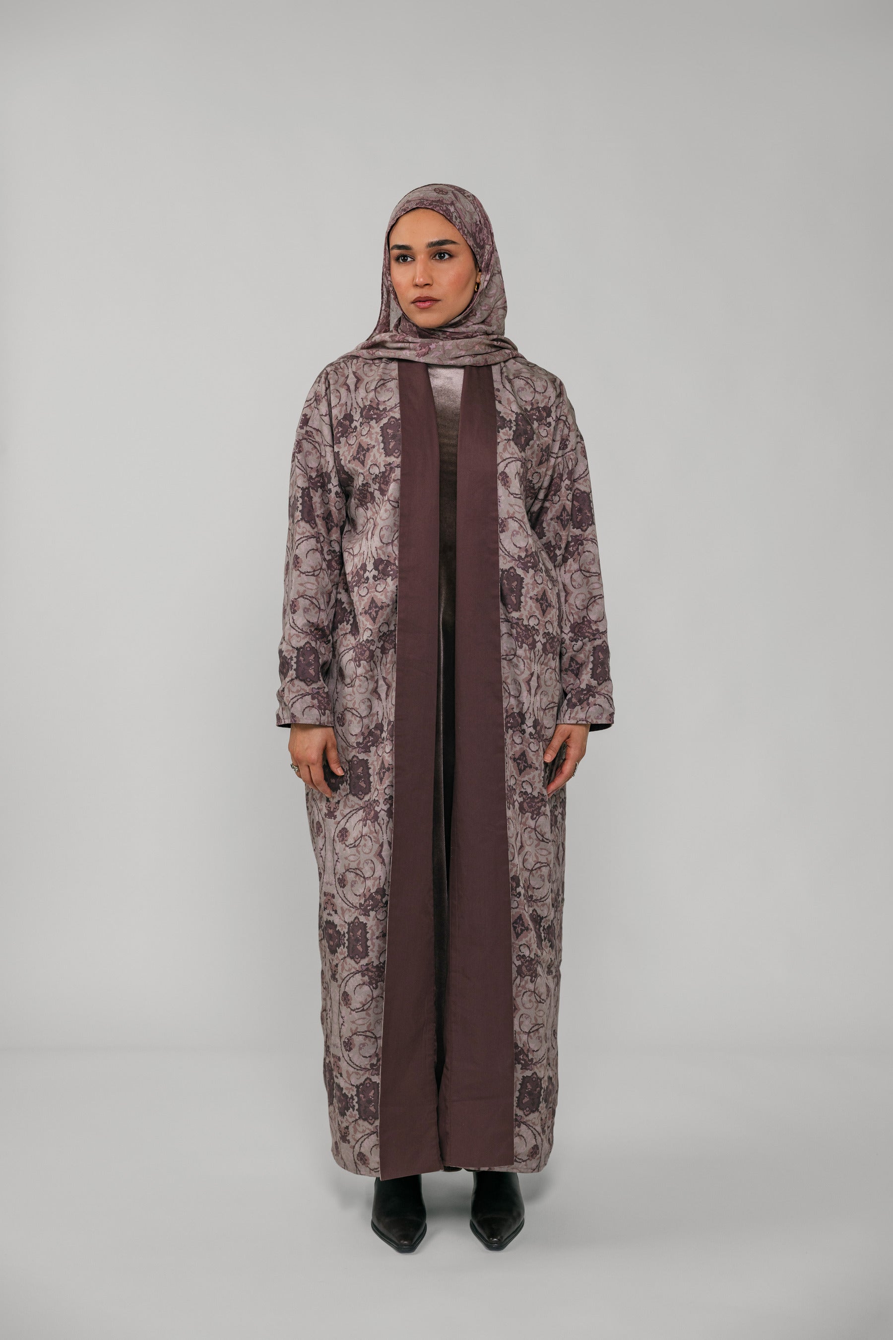 Woman wearing a long floral dress with a brown hijab on a gray background