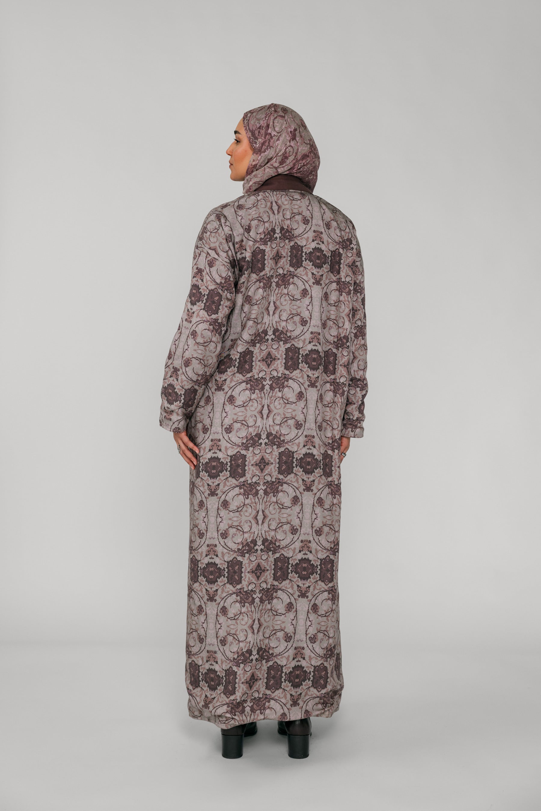Woman wearing a long floral-patterned abaya and hijab on a gray background