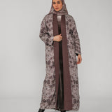 Woman wearing a long floral abaya with a brown floral hijab on a gray background