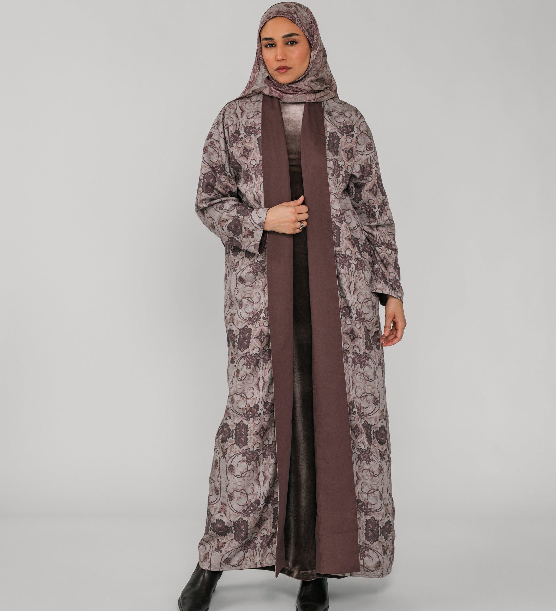 Woman wearing a long floral abaya with a brown floral hijab on a gray background