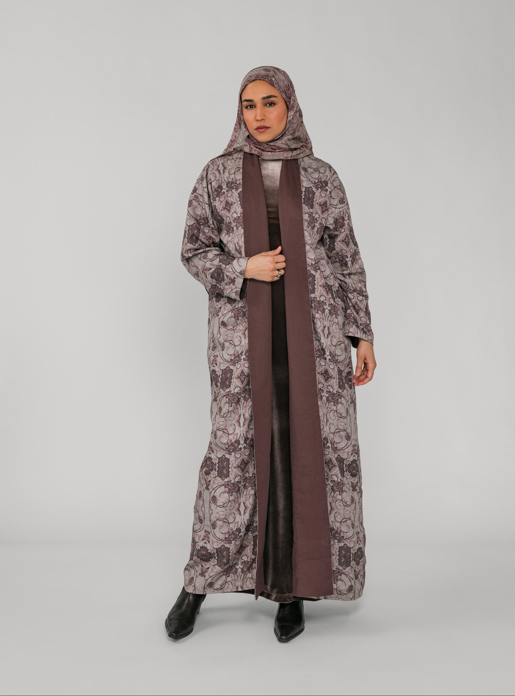 Woman wearing a long floral abaya with a brown floral hijab on a gray background