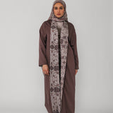 Woman wearing a brown abaya and patterned hijab on a gray background