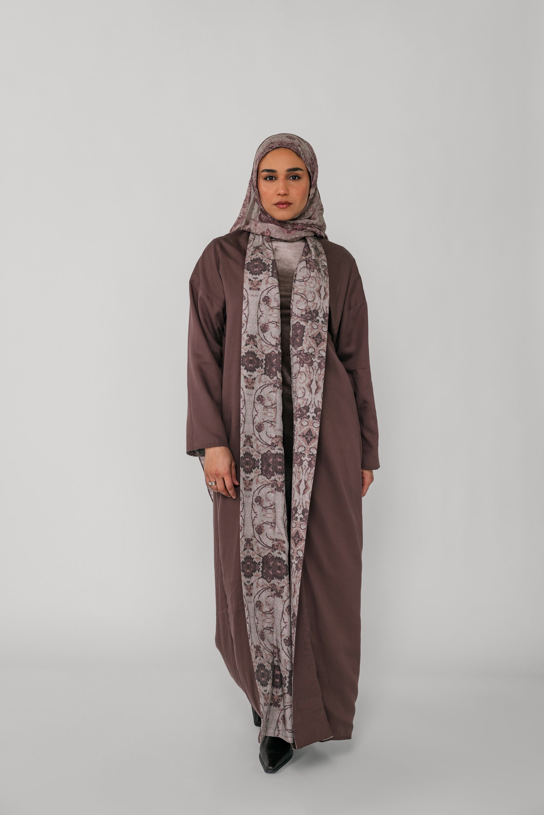 Woman wearing a brown abaya and patterned hijab on a gray background