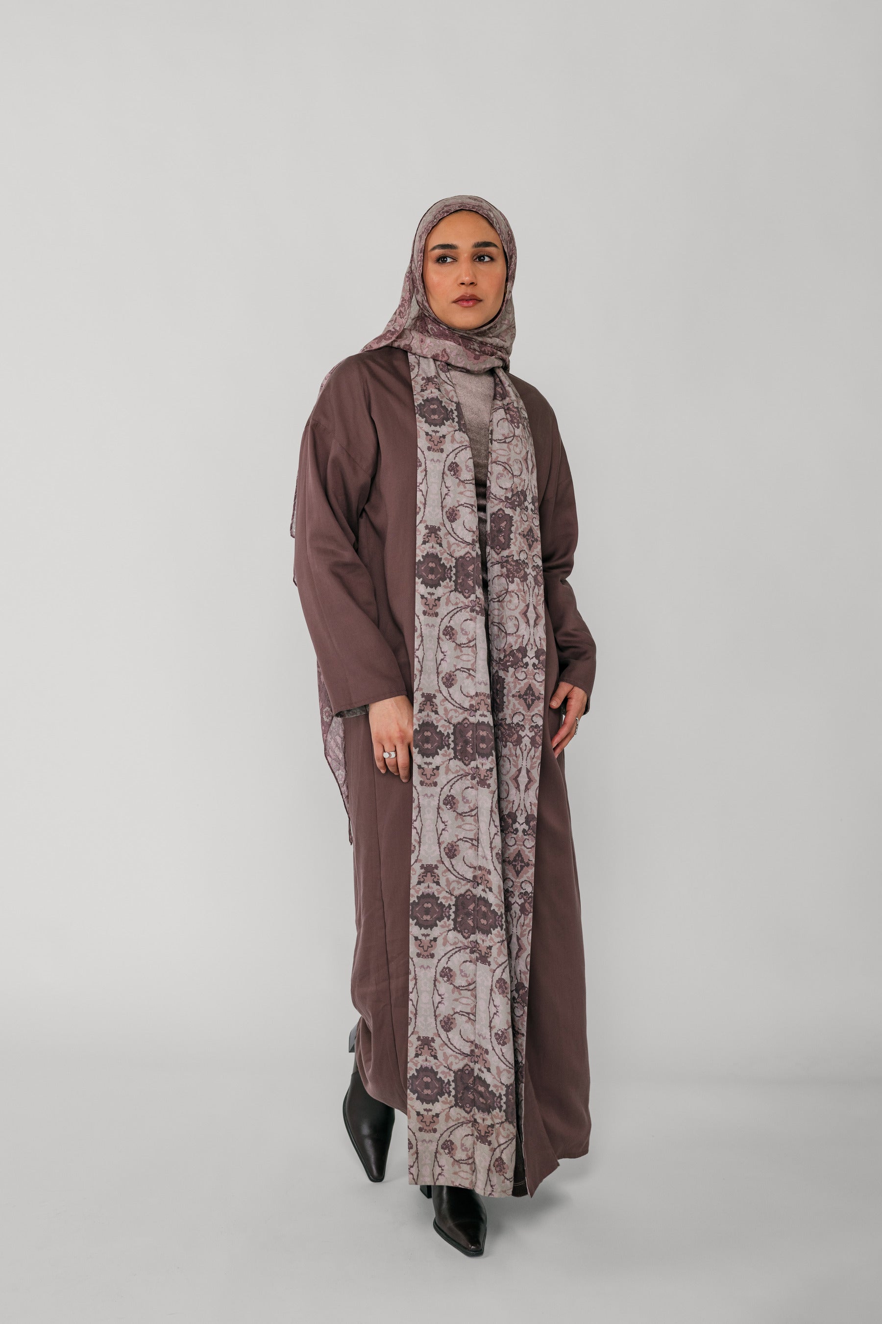 Woman wearing a long brown dress with a floral patterned scarf on a white background
