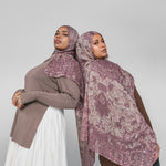 Two women wearing mauve patterned hijabs on a plain background
