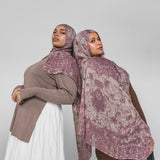 Two women wearing mauve patterned hijabs on a plain background