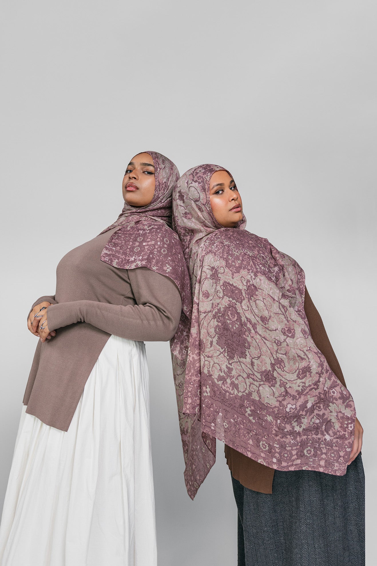 Two women wearing mauve patterned hijabs on a plain background