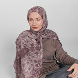 Woman wearing a patterned hijab, brown top, and gray skirt on a white background