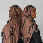 Two women wearing matching brown hijabs with black patterns against a white background