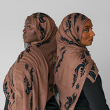 Two women wearing matching brown hijabs with black patterns against a white background