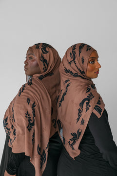 Two women wearing matching brown hijabs with black patterns against a white background