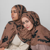 Two women wearing brown hijabs with black patterns on a white background