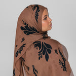 Woman wearing a brown hijab with black floral patterns on a plain background