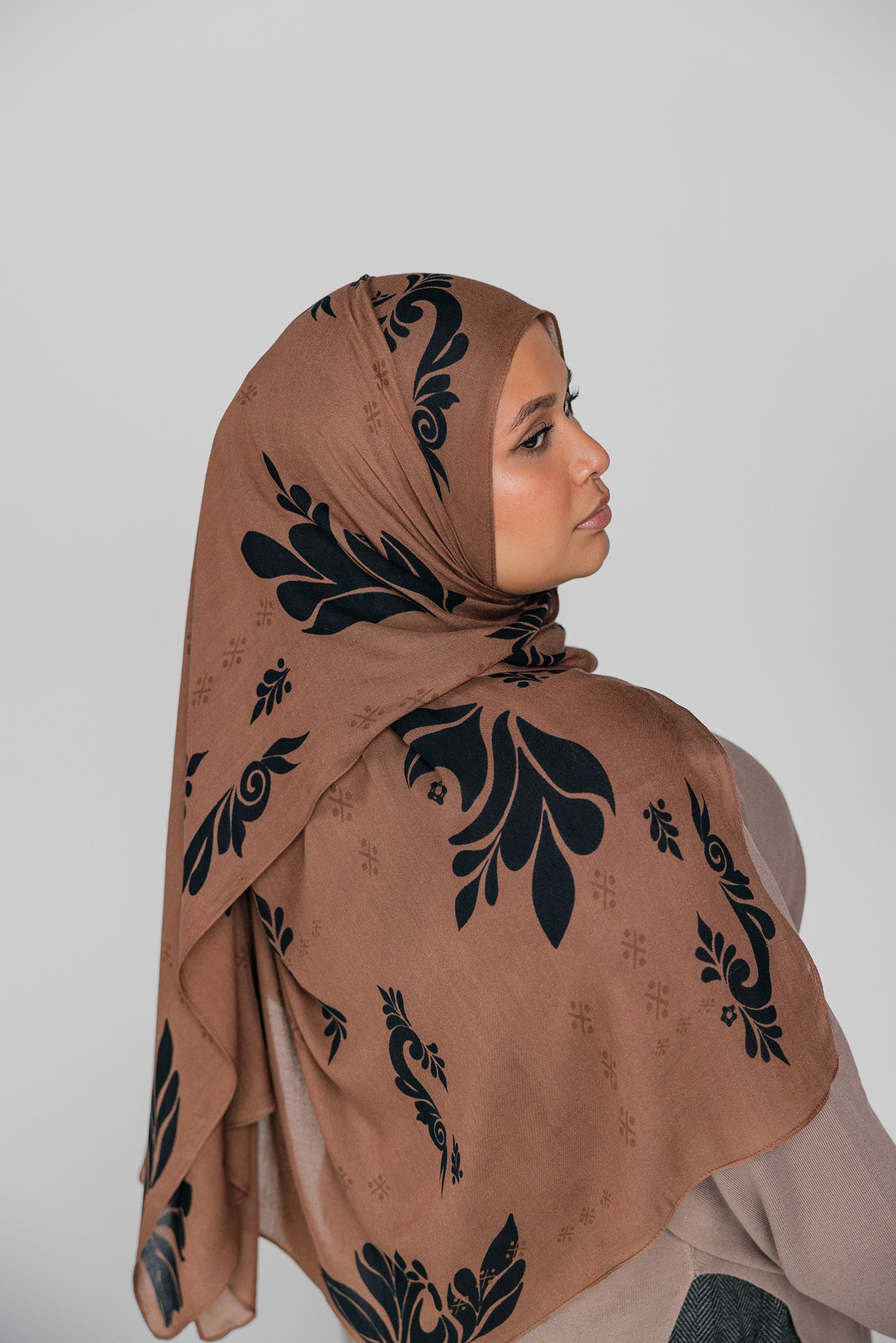 Woman wearing a brown hijab with black floral patterns on a plain background