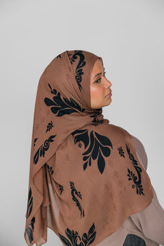 Woman wearing a brown hijab with black floral patterns on a plain background