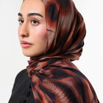A woman wearing a dark brown and black patterned hijab, photographed in profile against a clean light gray studio background.