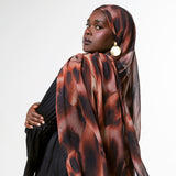 A woman wearing a black outfit and a brown and black patterned hijab, photographed against a plain light gray studio background.