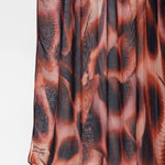 A close-up of a pleated fabric garment, likely a skirt, featuring an abstract animal-inspired print in shades of rust orange, brown, and charcoal gray.