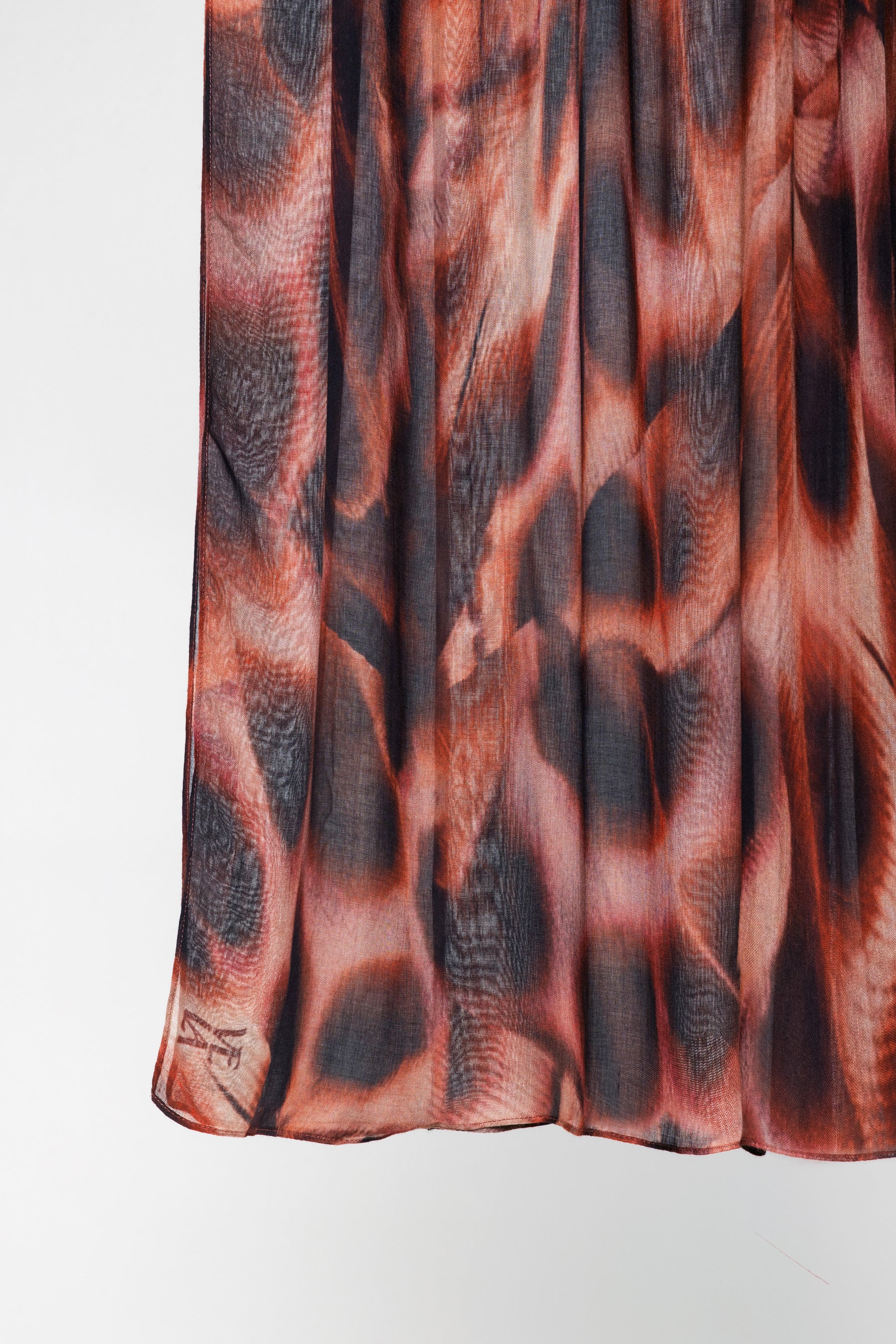 A close-up of a pleated fabric garment, likely a skirt, featuring an abstract animal-inspired print in shades of rust orange, brown, and charcoal gray.