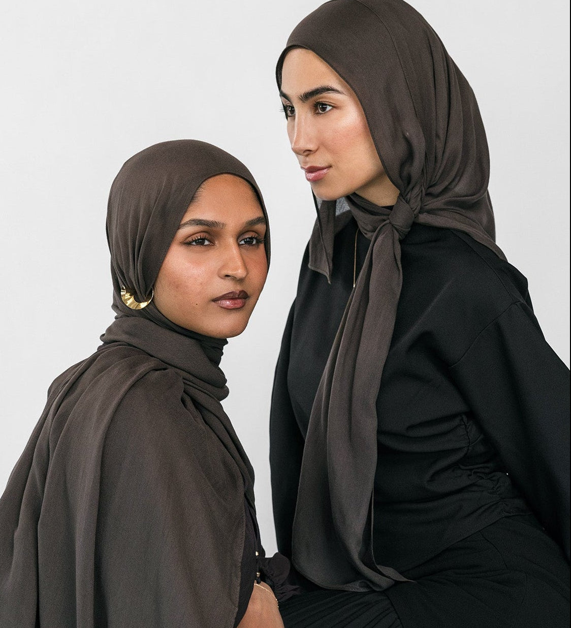 Two women wearing hijabs and black clothing against a white background