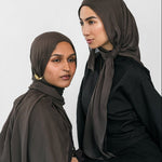 Two women wearing hijabs and black clothing against a white background
