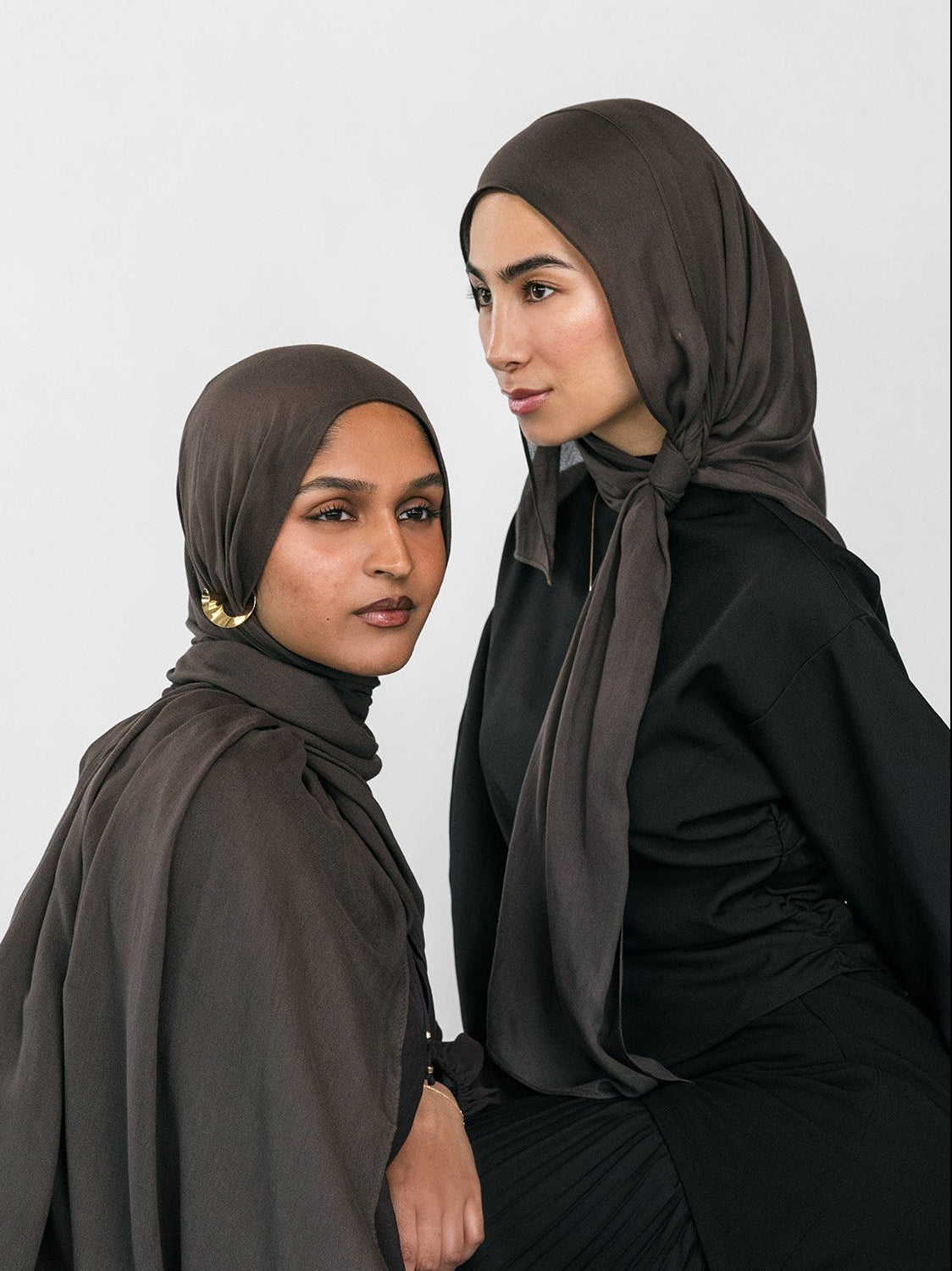 Two women wearing hijabs and black clothing against a white background