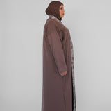 Woman wearing a long brown dress with a matching hijab on a white background