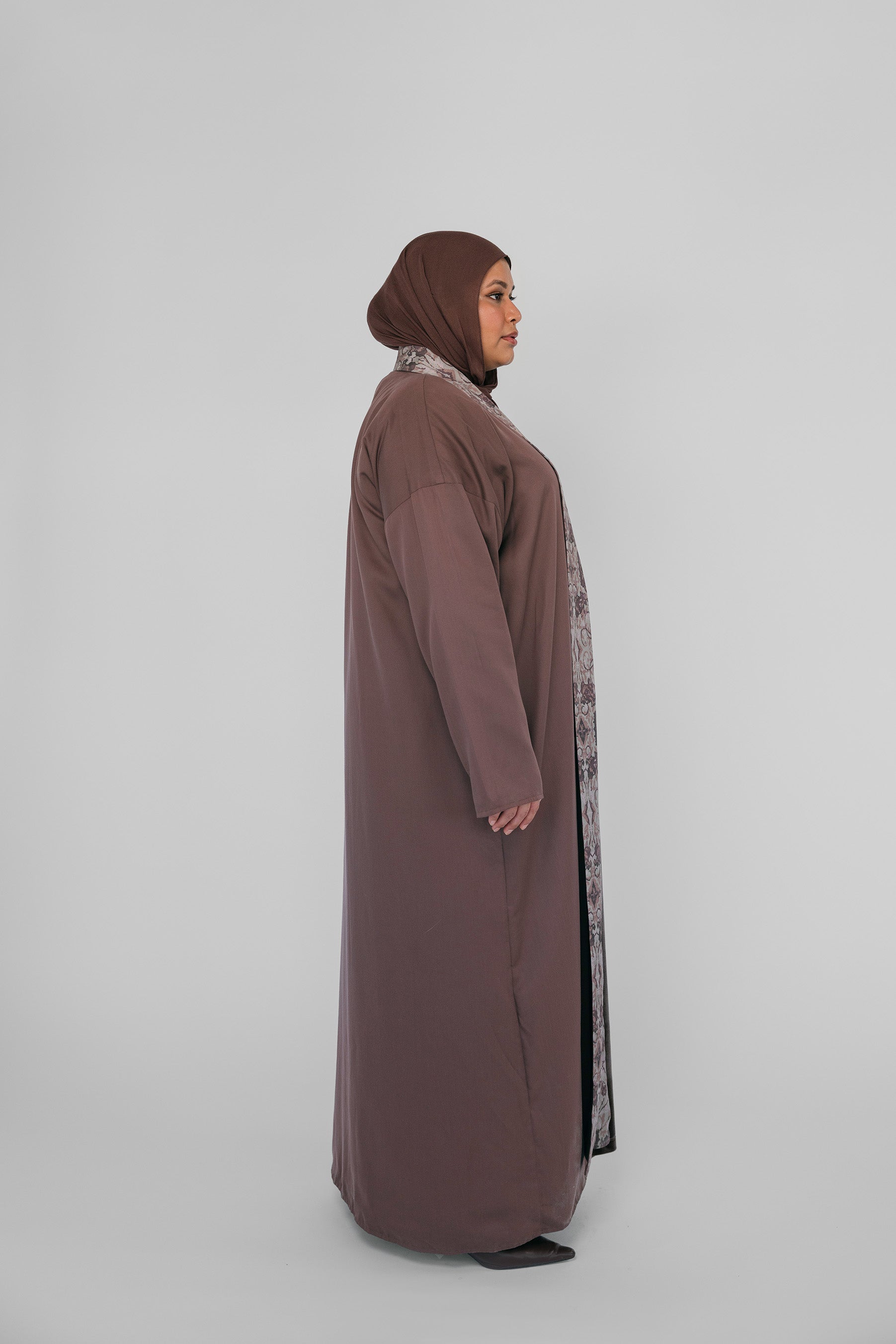 Woman wearing a long brown dress with a matching hijab on a white background