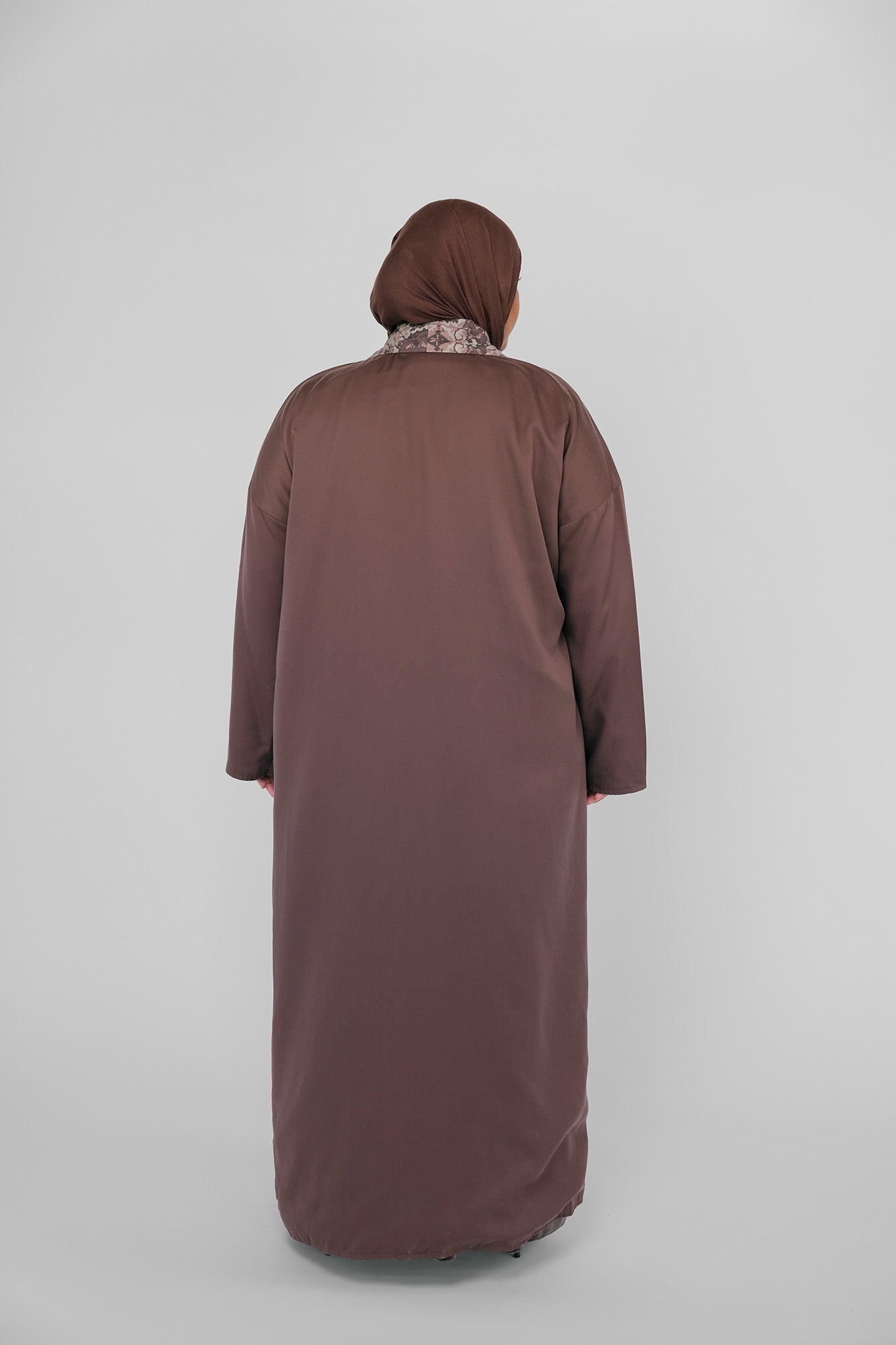 Person wearing a long brown abaya and hijab on a white background
