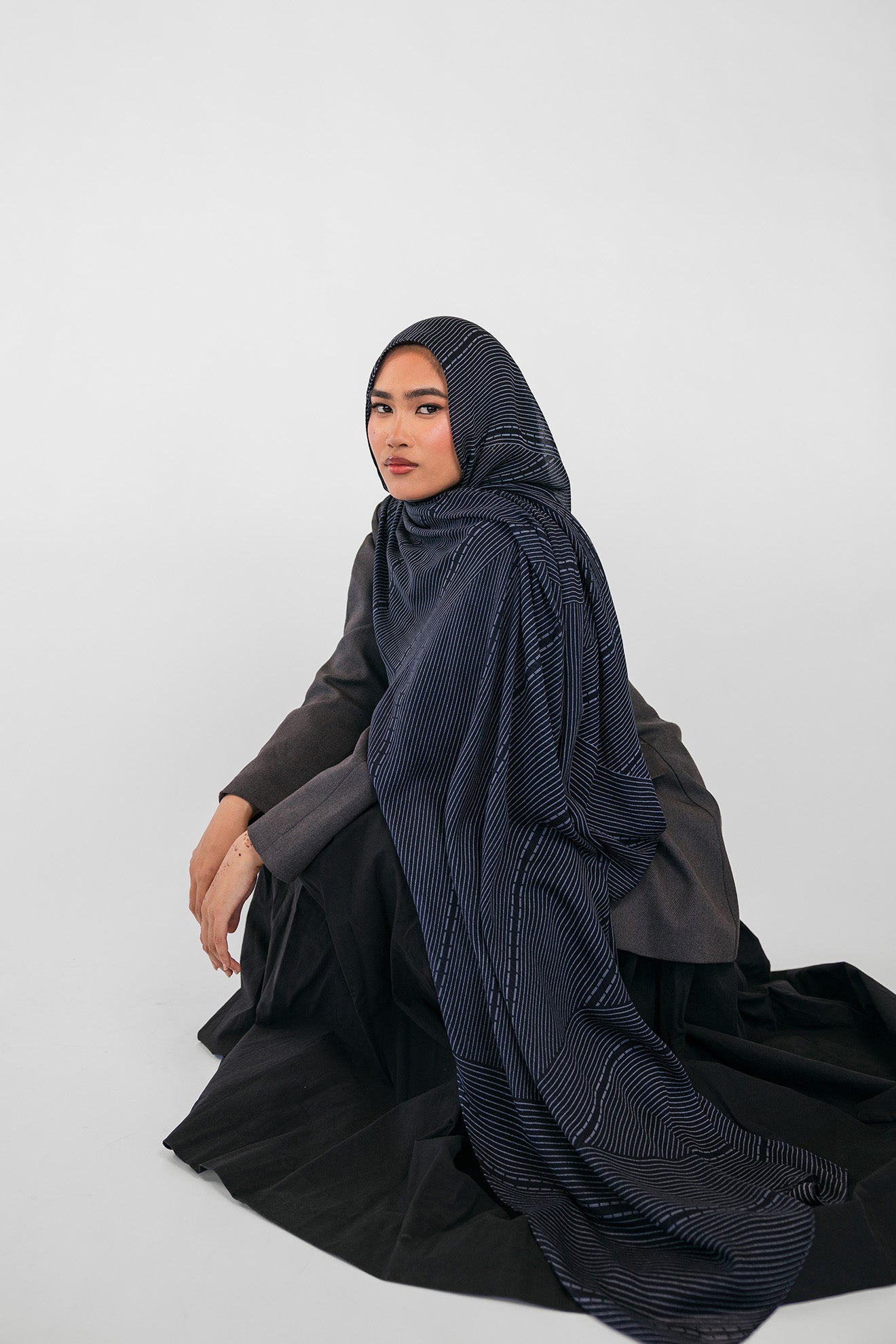 Woman wearing a dark blue hijab and black outfit on a white background