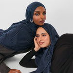 Two women wearing navy striped hijabs on a white background