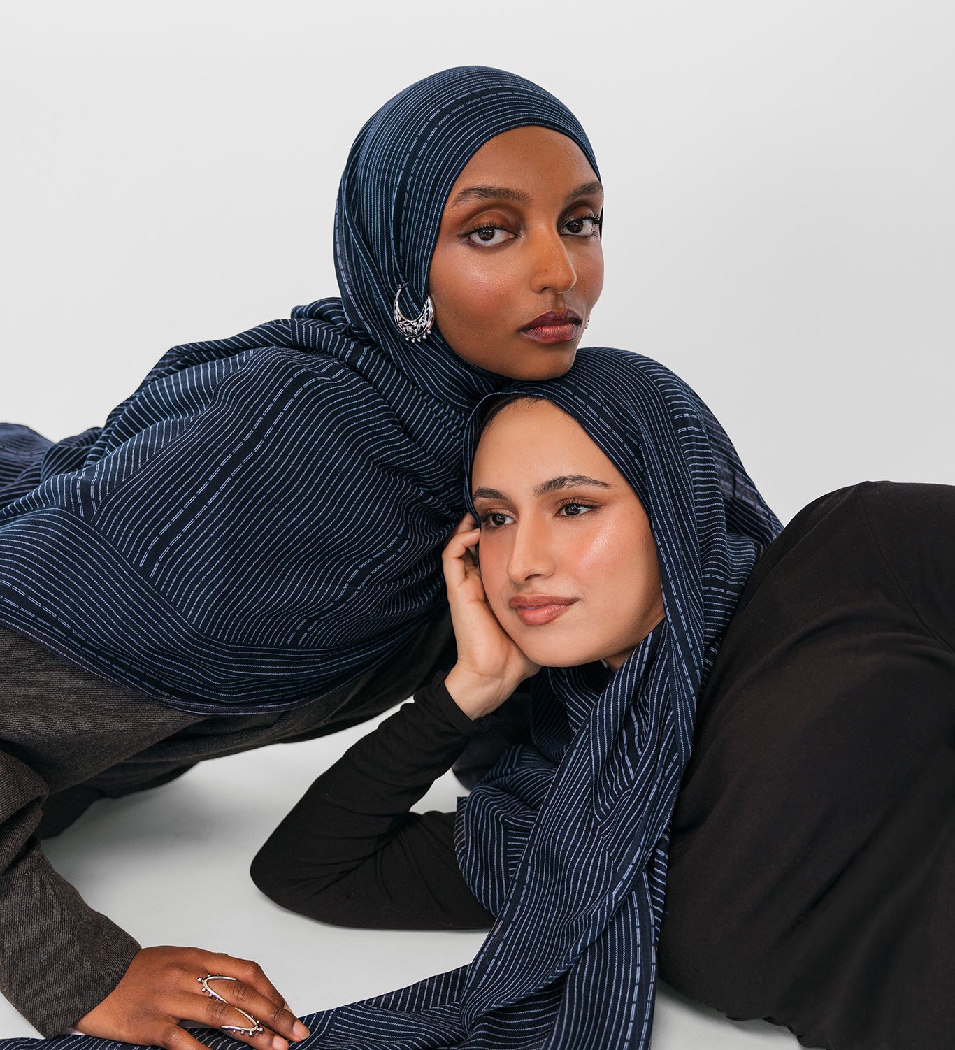 Two women wearing navy striped hijabs on a white background